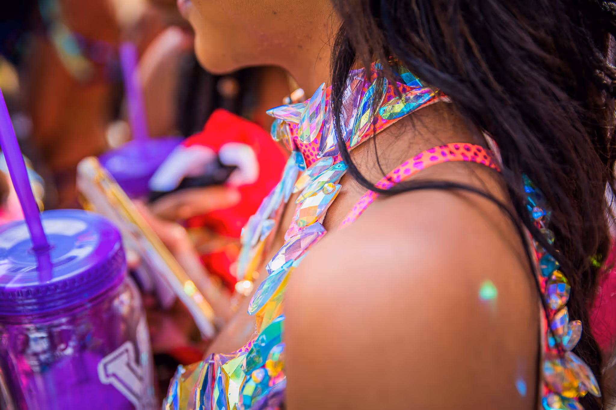 Close-up of a person wearing colorful reflective costume pieces with long dark hair, holding a purple cup with a straw.