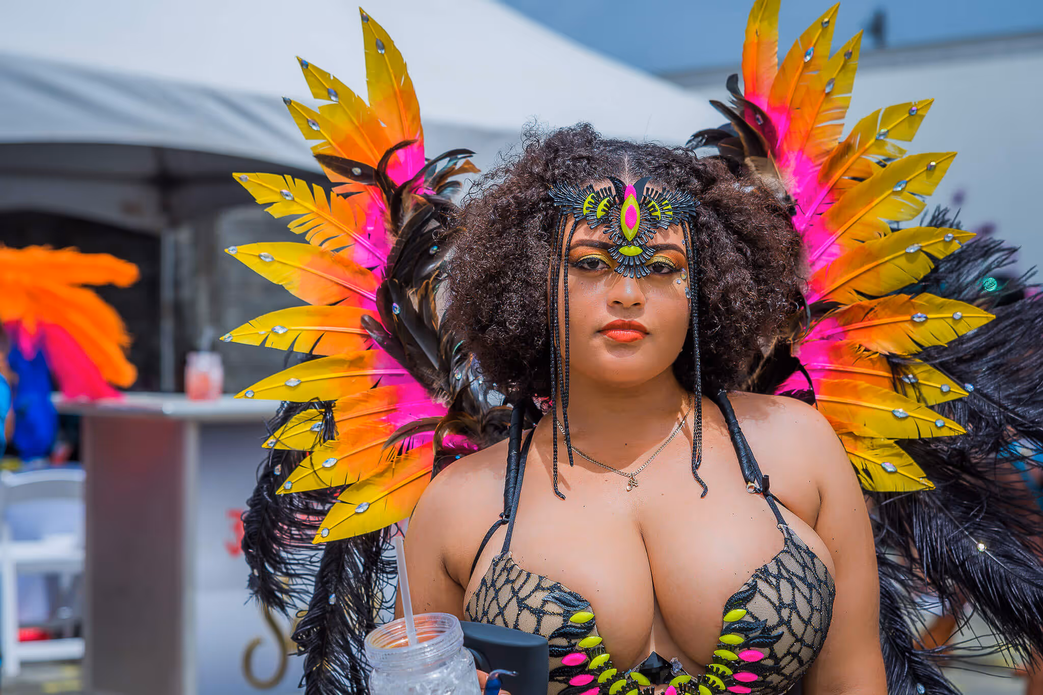 Woman wearing vibrant carnival costume with yellow and pink feathers and elaborate face decoration.