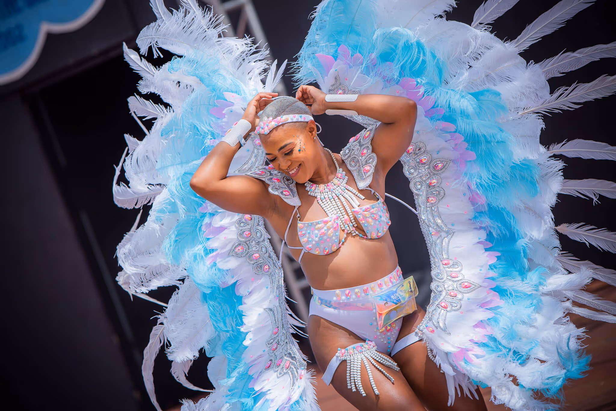 Smiling dancer wearing a vibrant carnival costume with large blue and white feathered wings and beaded accessories.