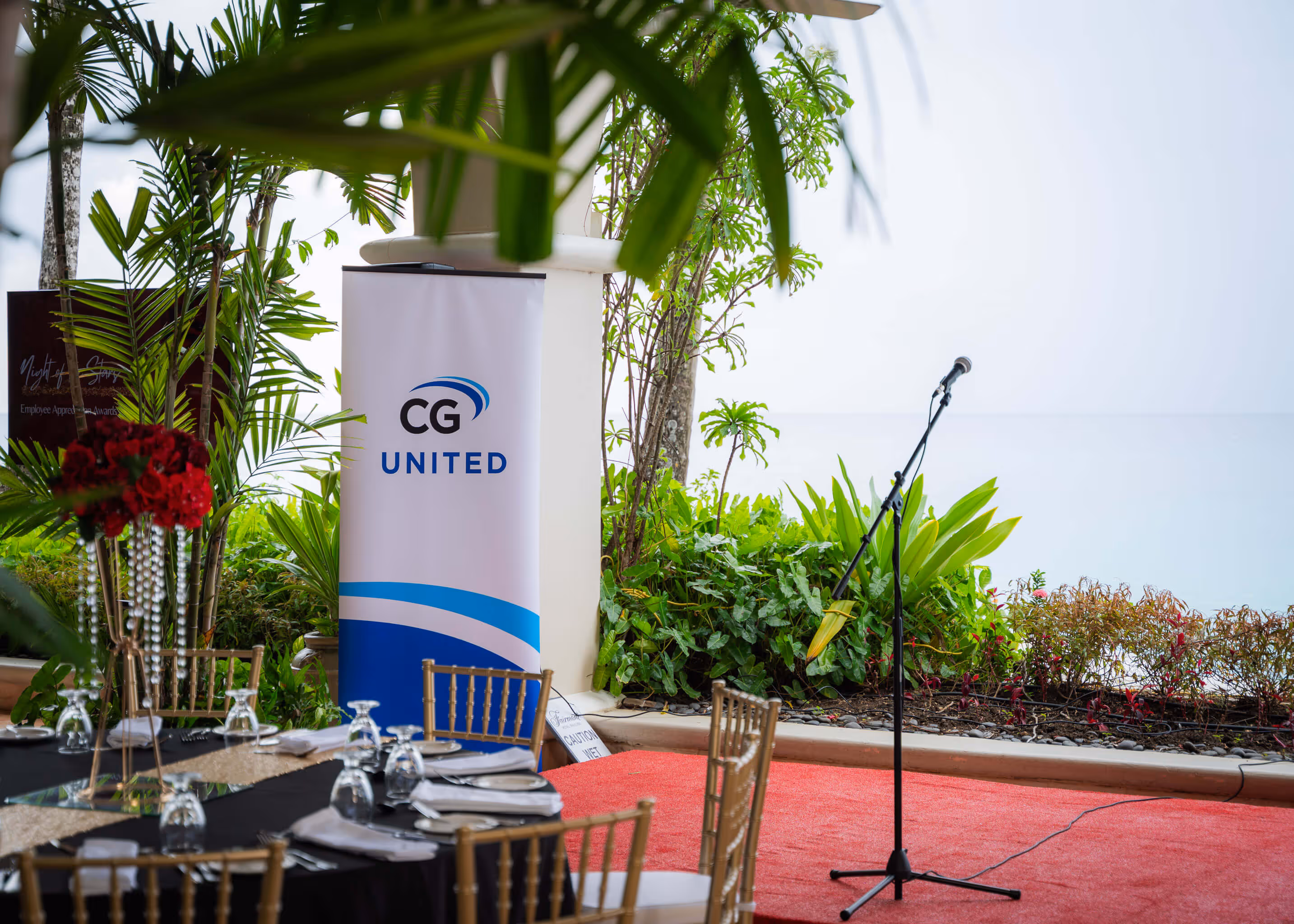 Microphone stand on a red carpeted stage near plants and a CG United banner in an outdoor event setup.