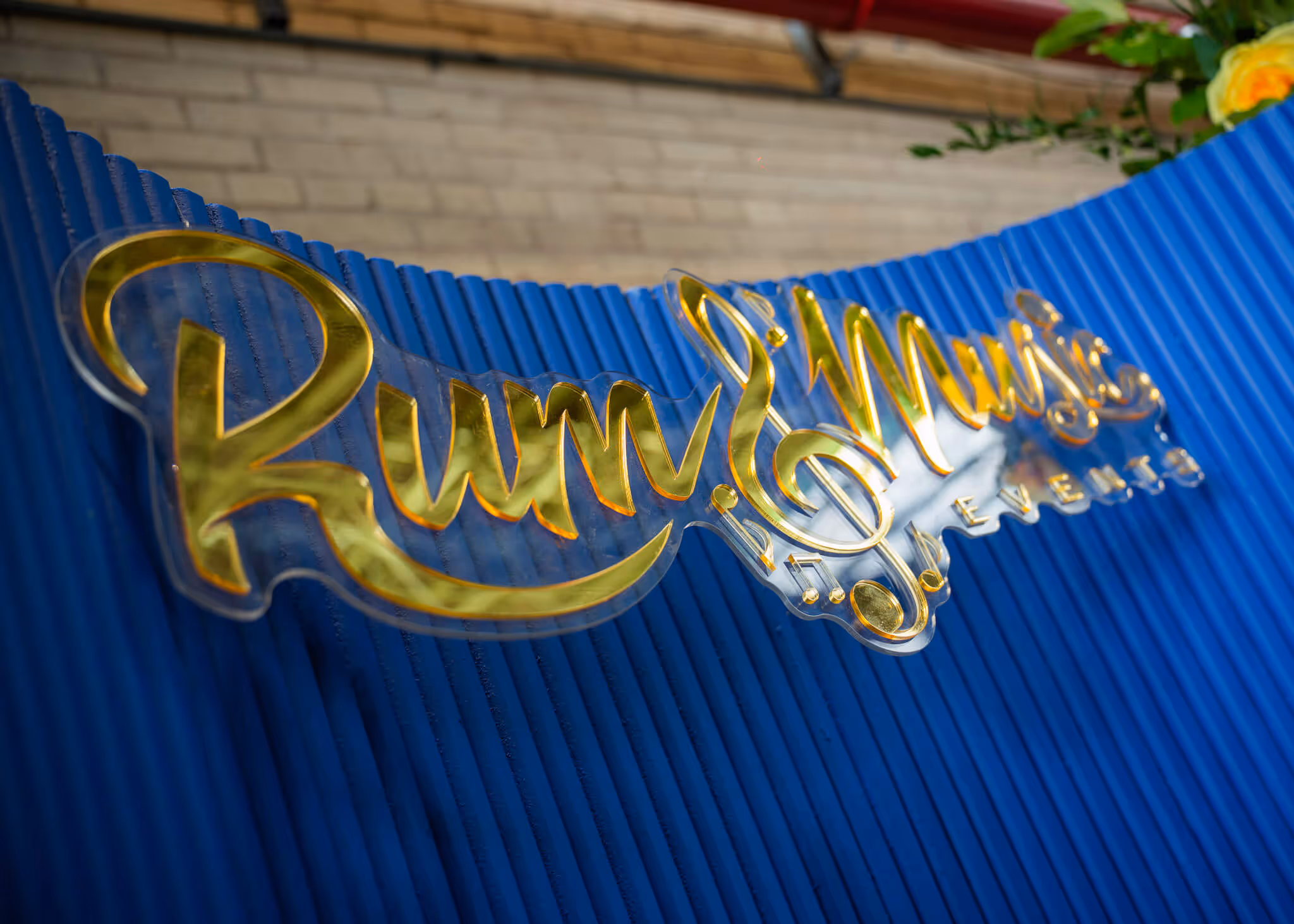 Gold cursive sign reading 'Rum & Music' mounted on a blue ribbed wall.