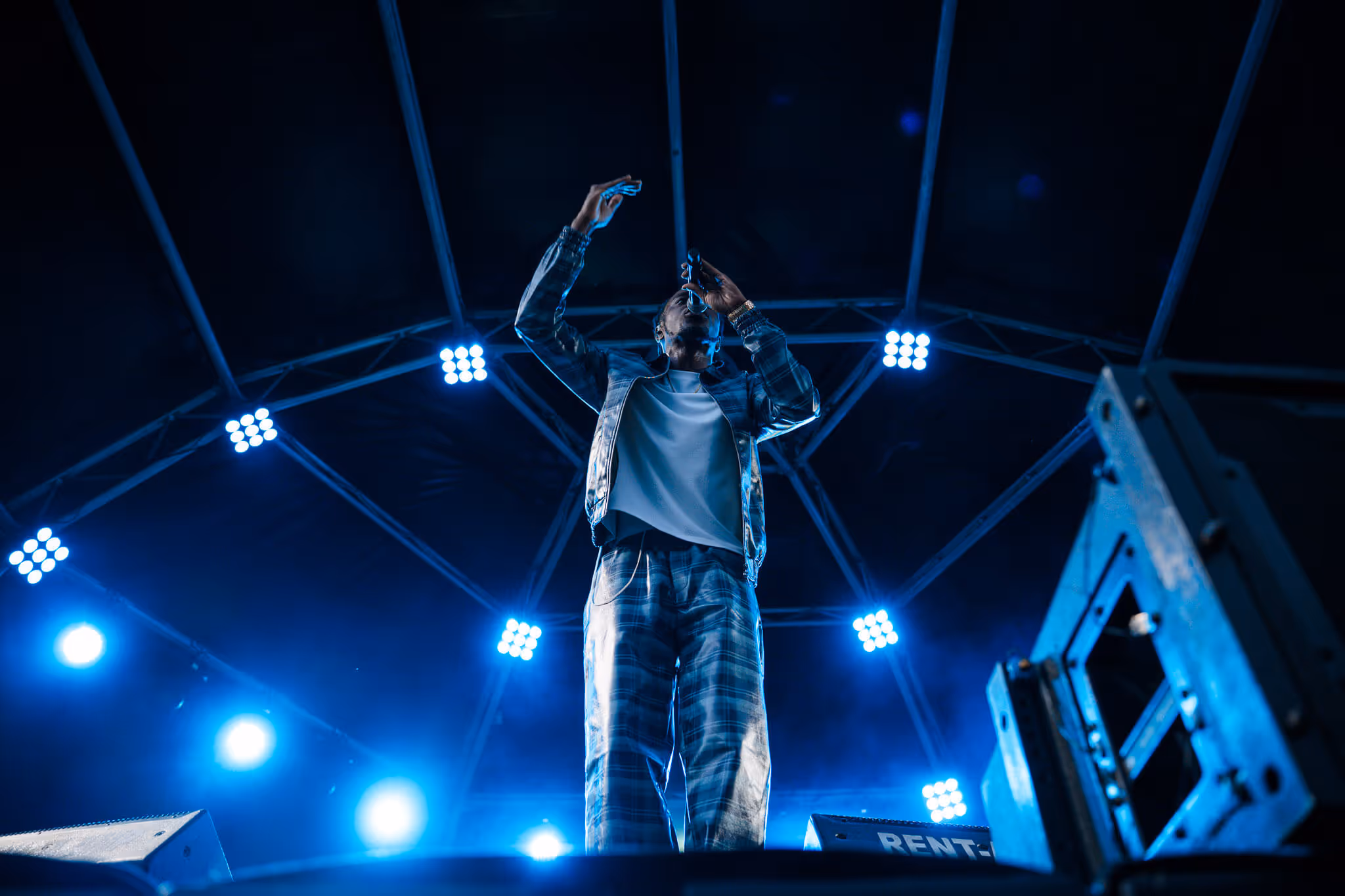 Performer singing on stage under blue lights with raised hand in a dark venue.