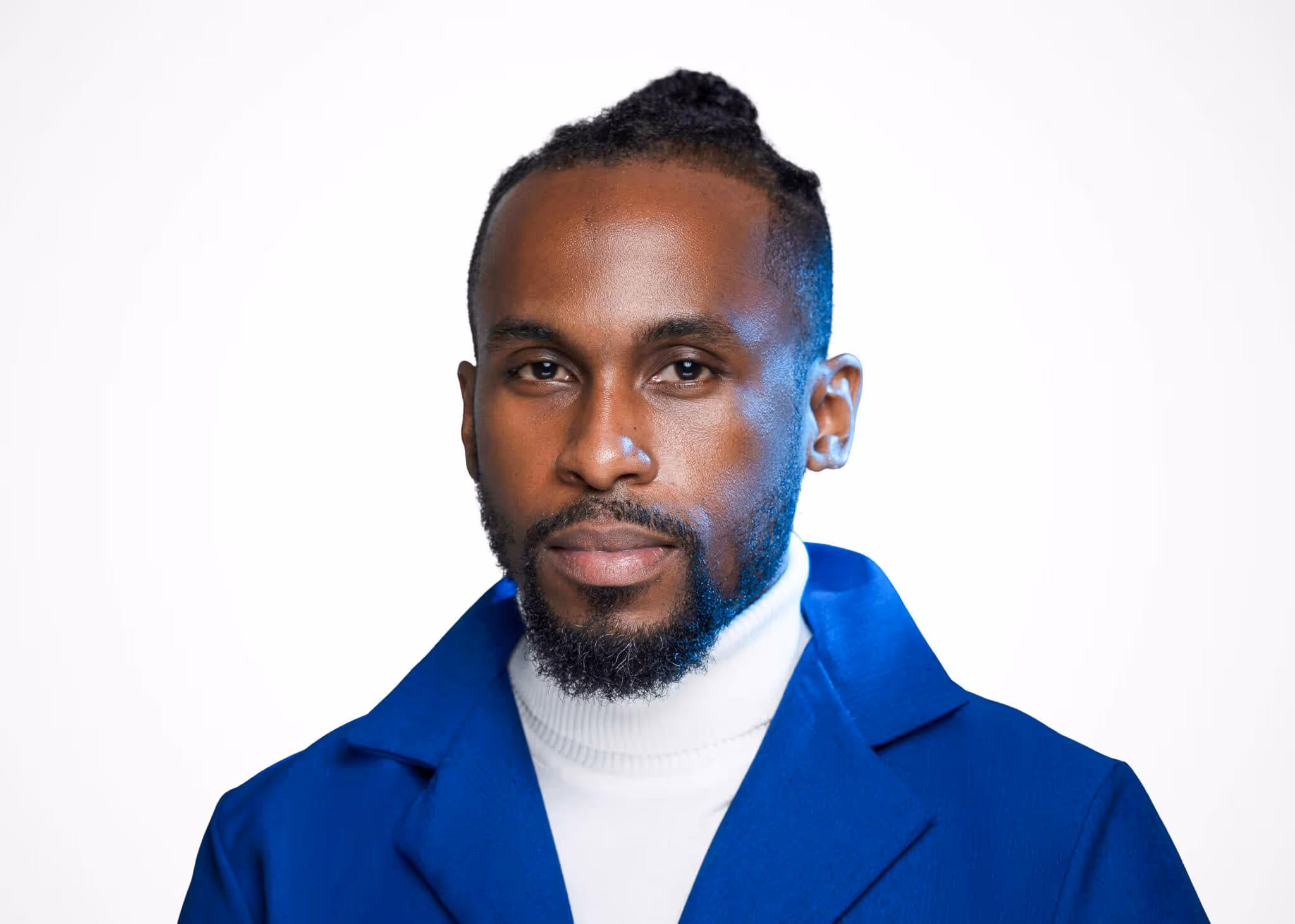 Portrait of a man with a beard and mustache wearing a white turtleneck and blue jacket against a white background.
